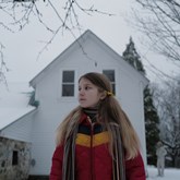 A girl stands outside a white house
