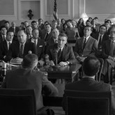Oppenheimer in a room of other men in black and white