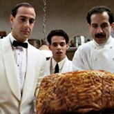 Big Night - three men in white look at a large piece of cooked meat