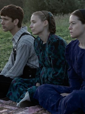 A still from Women Talking with three characters sat on a picnic rug, sombrely dressed and serious.
