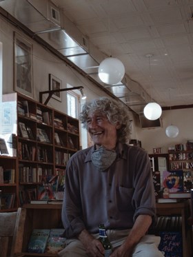 Hello Bookstore film still. a man sits laughing in a book shop 