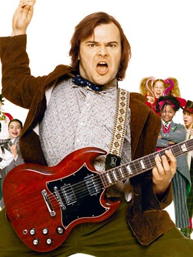 School of Rock - man playing guitar with children stood behind him dressed rock themed clothing.