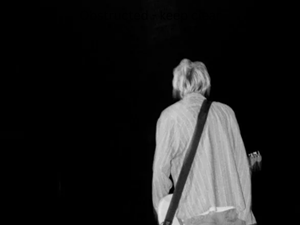 kurt cobain stands on stage, his back to the camera
