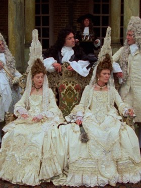 A group of people in old fashioned clothing sit in a fancy room.